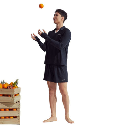 Man in black Speedo Wavechasers 2.0 long sleeve polo with UPF50+ sun protection, juggling an orange.
